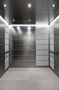 FSRT735 Интерьер лифта Levele-103 с главными панелями из нержавеющей стали, отделка морским камнем; акцентные панели из стекла vivichrome chromis, прослойка белого цвета, стандартная отделка; потолок лифта со светодиодными светильниками и светодиодным акц